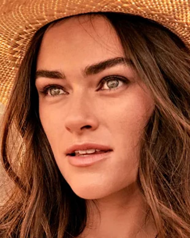 Myla Dalbesio poses in front of the bright yellow leaves in a tan straw cowgirl hat.